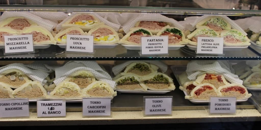 A bunch of food is on display in a store, with Sandwich and Tramezzino