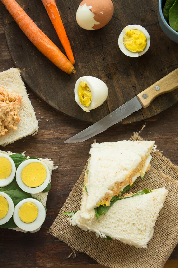 A cut in half sandwich sitting on top of a wooden cutting board, with Bread and eggs