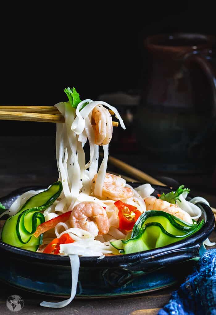 Rice noodles and shrimp on chopsticks over the Thai salad bowl.