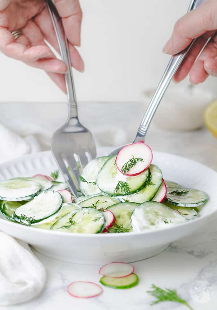 Tossing the cucumber salad with sour cream and dill.