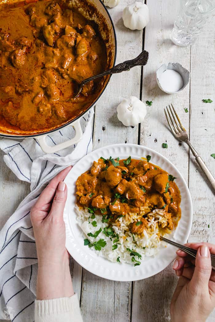 Chicken masala dish in a white bowl and the pan, hands around the plate.